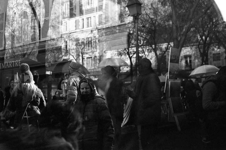 Double-exposure crowd in Montmartre — a figure with flowing hair beneath a pom-pom beanie